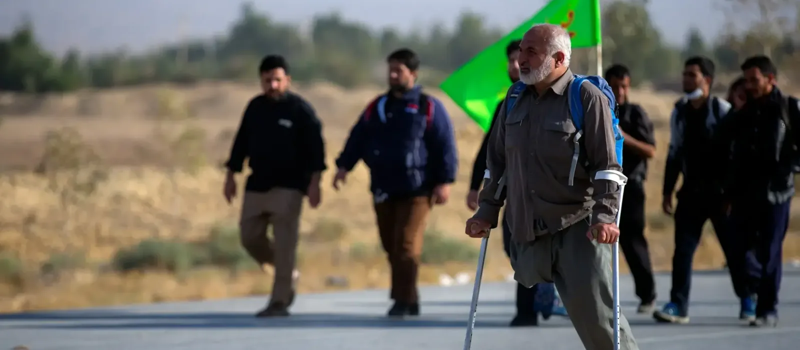 Walking group on a country road led by an older man using a forearm crutch