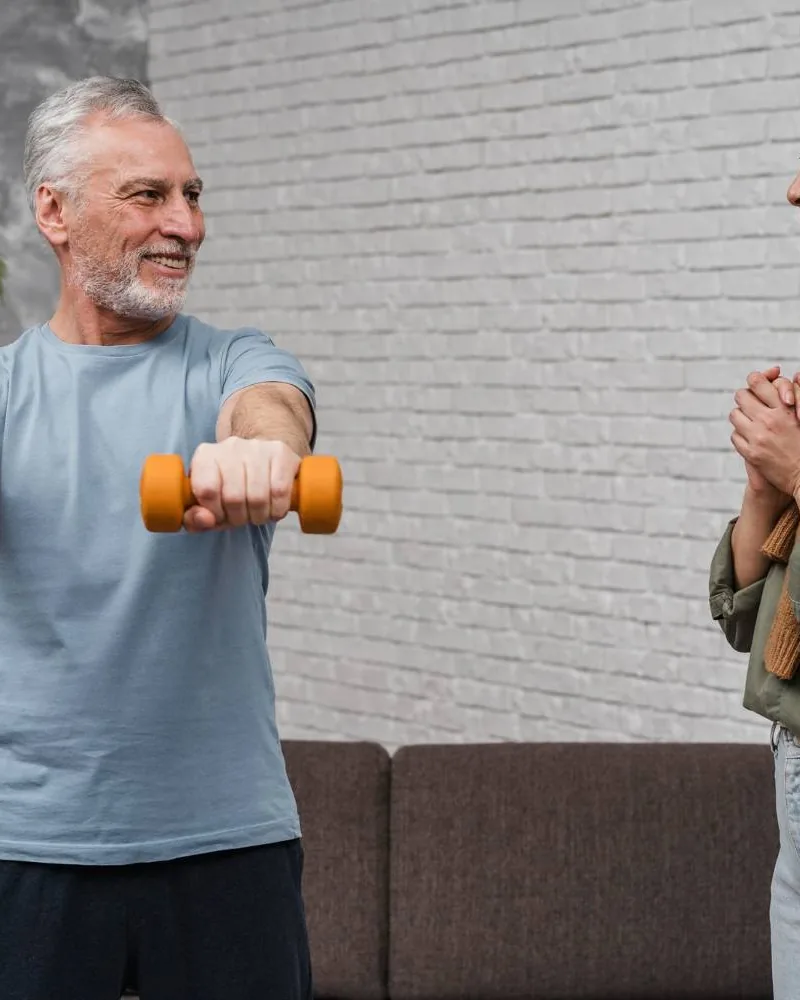 Older man lifting dumbbells while a therapist coaches his form