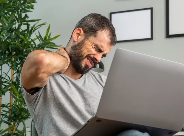 Man at a laptop gripping his neck and shoulder in pain