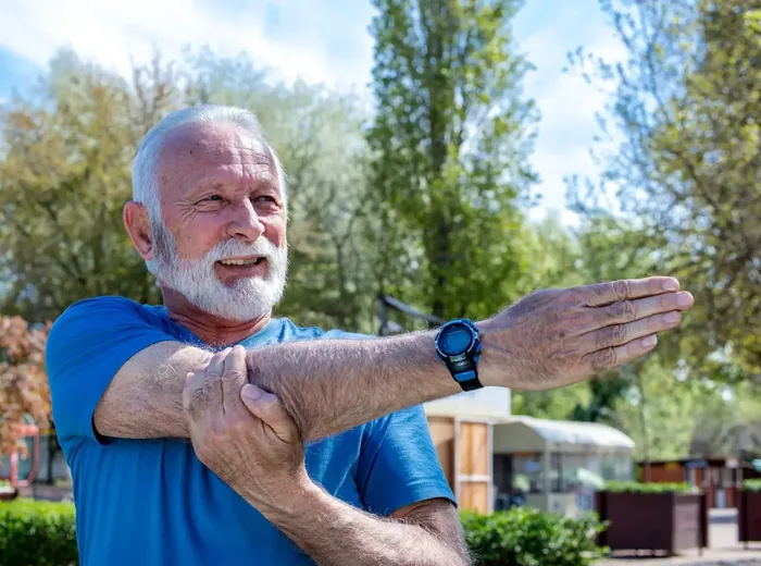 Older man outdoors pulling his arm across his chest in a shoulder stretch