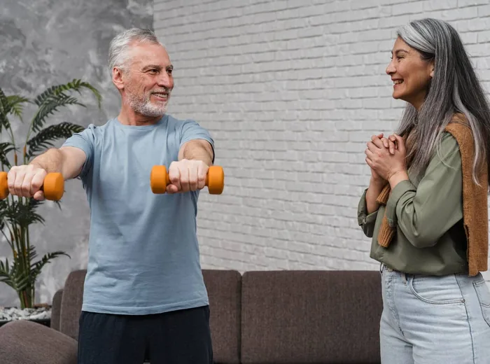 Older man lifting dumbbells while a therapist coaches his form