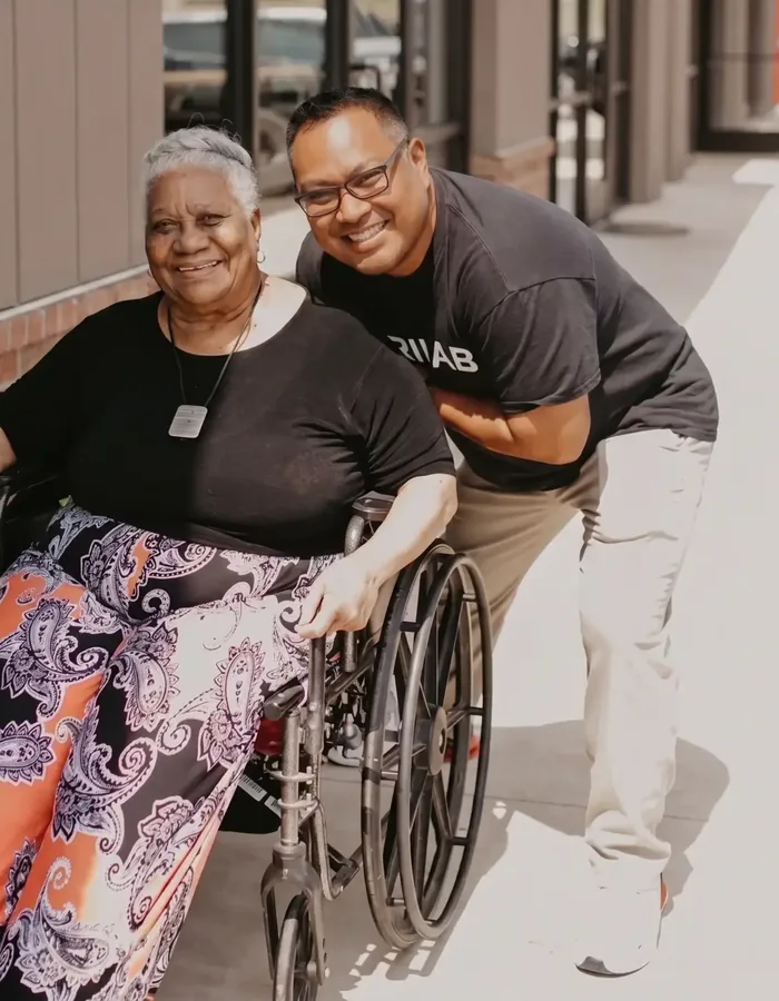 Dr. Michael Chua crouched beside a smiling patient in a wheelchair outside the clinic entrance